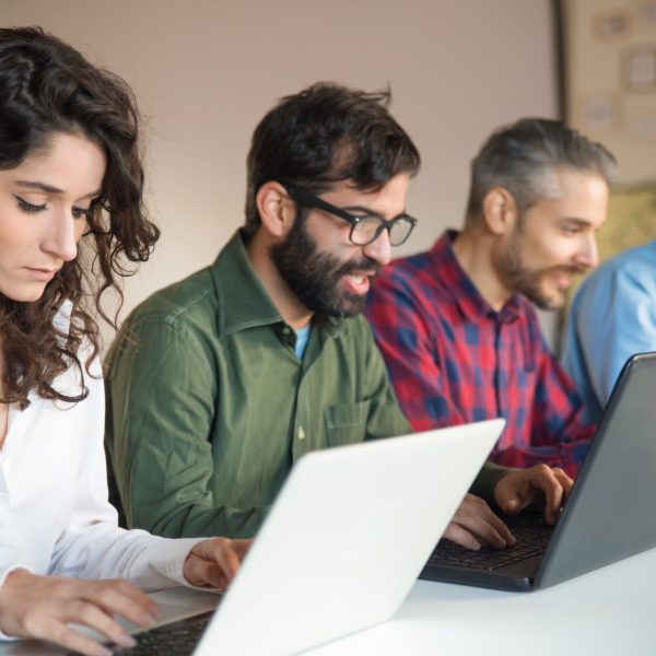 Focused coworkers using laptops at meeting table. Business colleagues in casual working together in contemporary office space. Communication concept